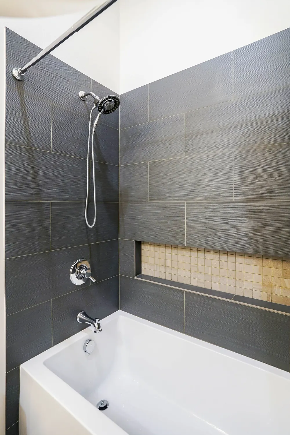 Tub-shower with dark gray tile and a recessed niche