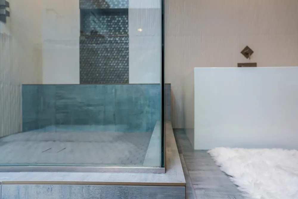 Glass shower with a blue glass tile band next to a white soaking tub