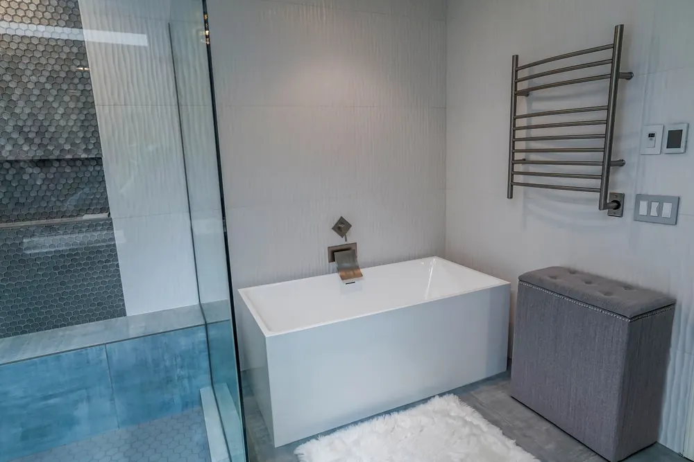 Soaking tub beside the glass shower, with a towel warmer