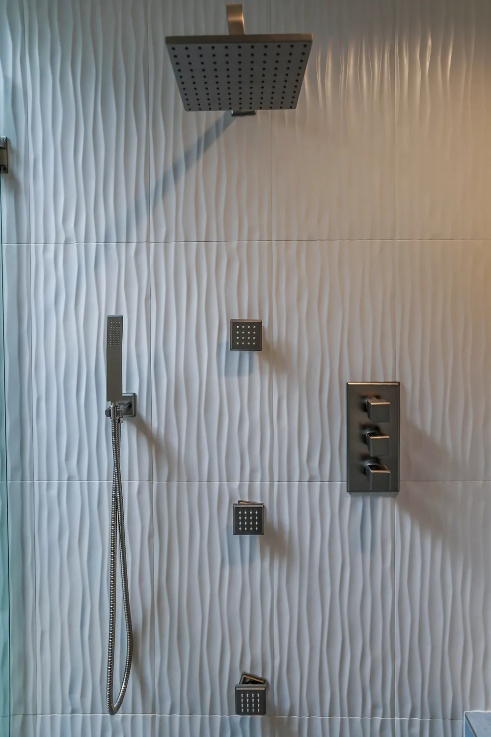 Shower wall with textured white tile, body sprays and handheld shower