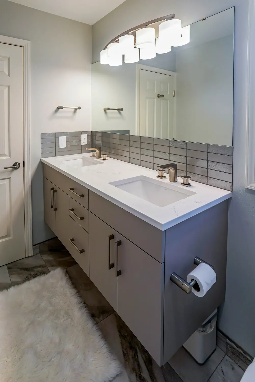 Gray vanity with a tile backsplash and wall lights