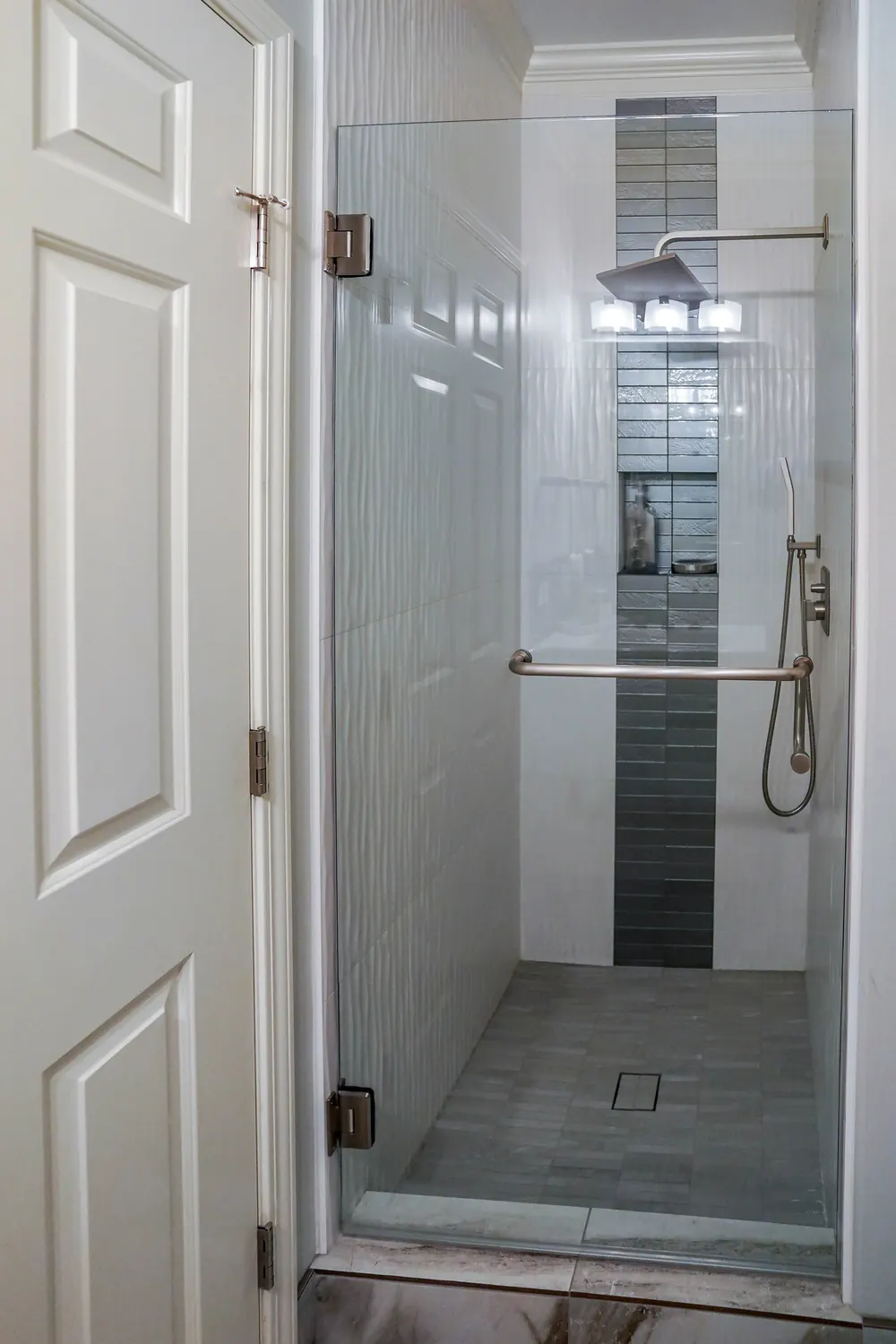 Shower with a glass door and a tall mosaic tile accent