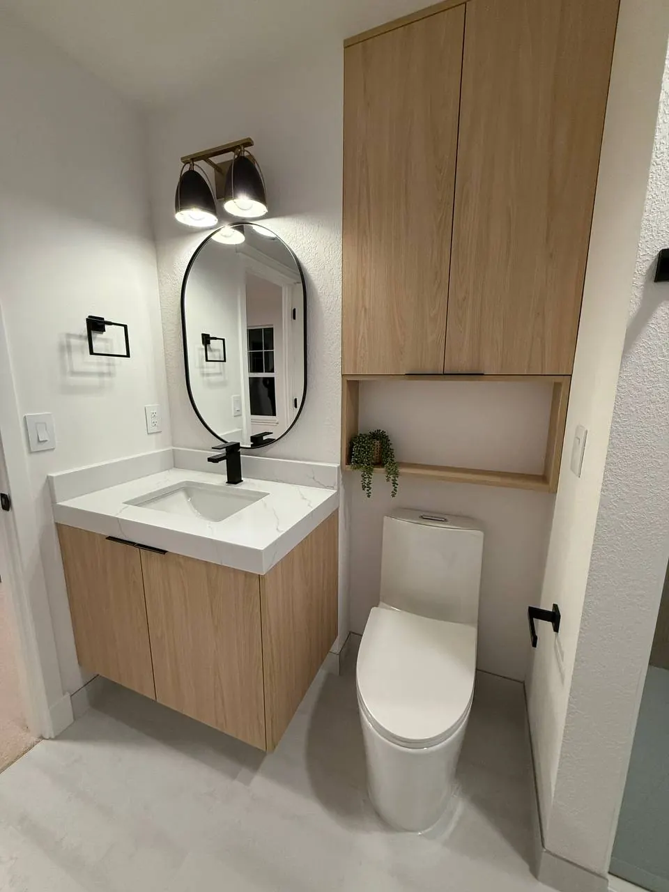 Small bath with a wood vanity, oval mirror and tall wood cabinet
