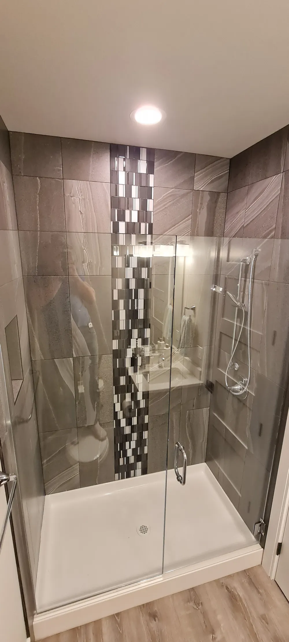 Shower with large gray tile, a mosaic stripe and glass door