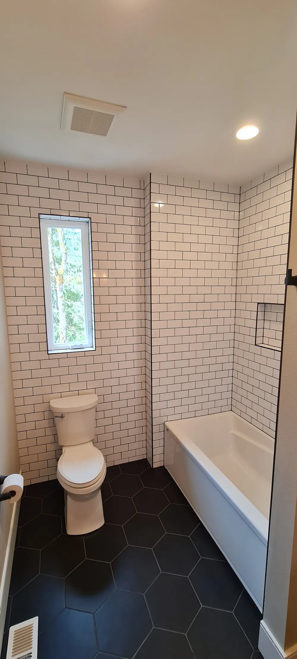 Bathroom with white subway tile, a black hexagon floor and a tub