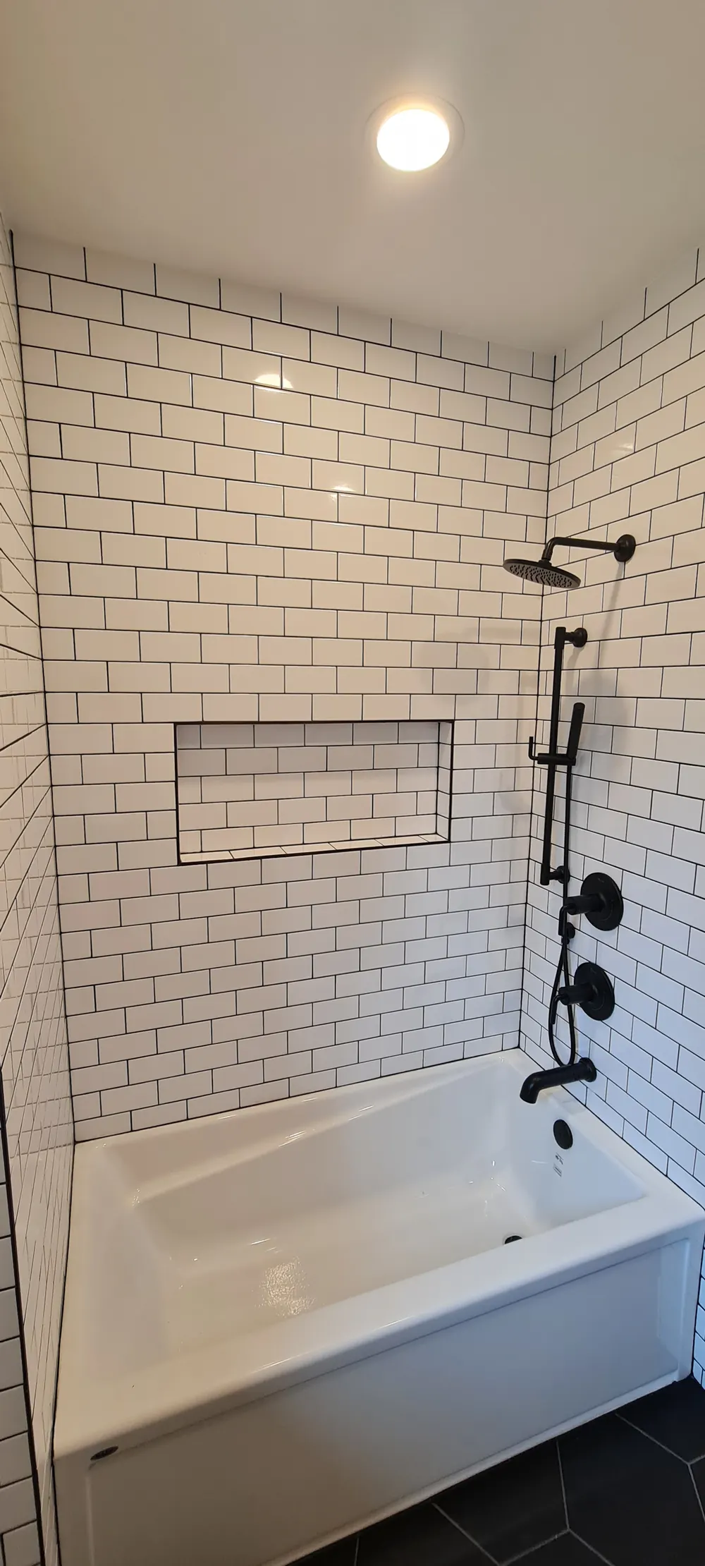 Tub surround in white subway tile with black fixtures and a niche