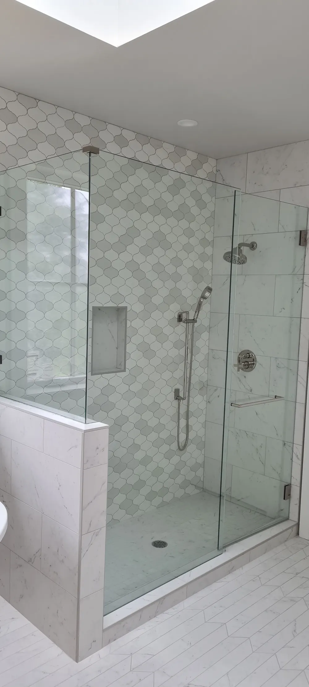 Glass shower with herringbone marble-look tile and a knee wall