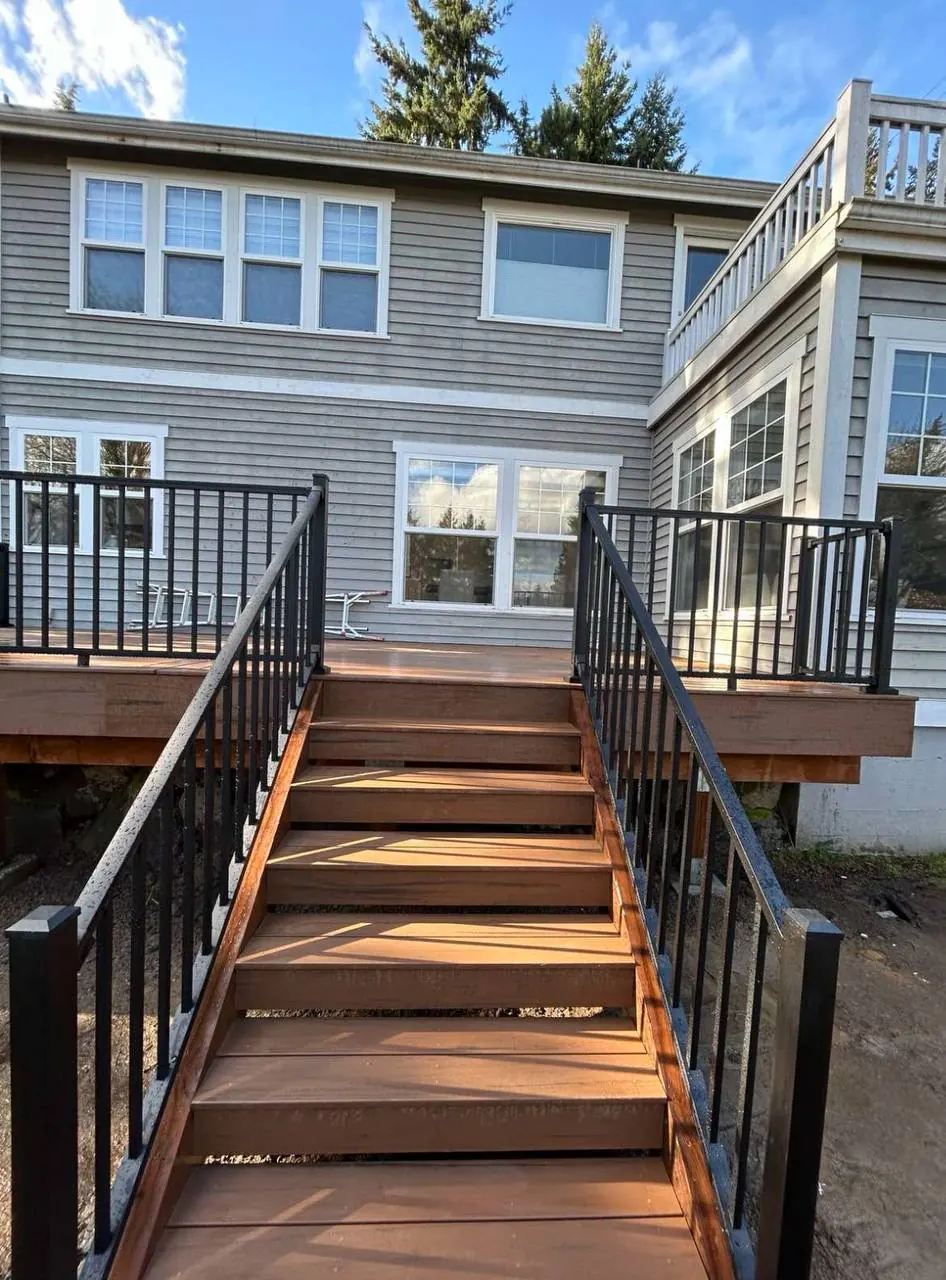 Deck stairs with black metal railings behind a gray-sided house