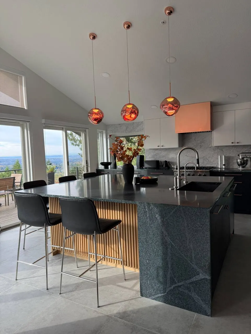 Black kitchen island with a stone waterfall end and copper pendants