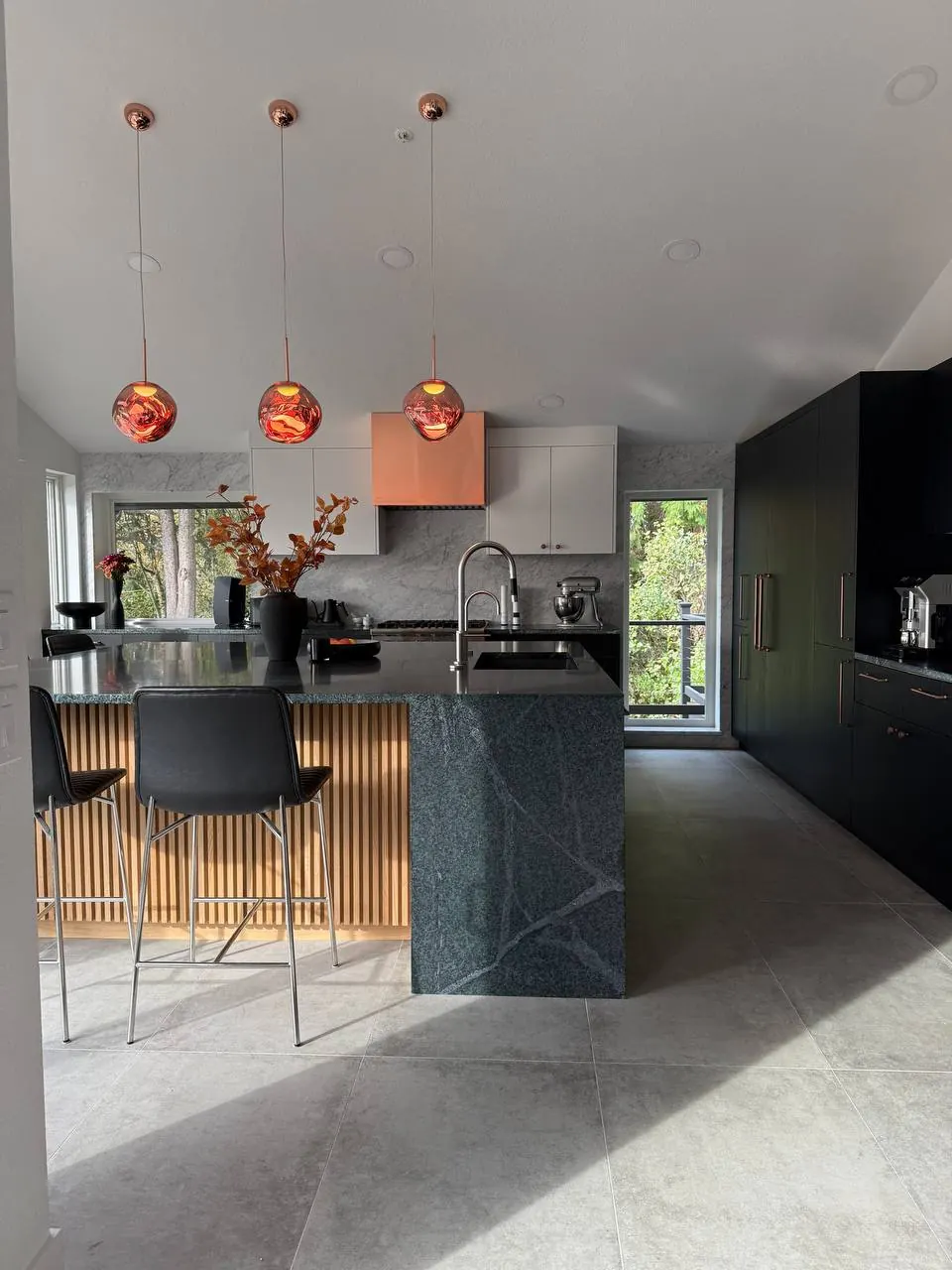 Kitchen with black cabinetry, a wood-slat island base and copper pendants