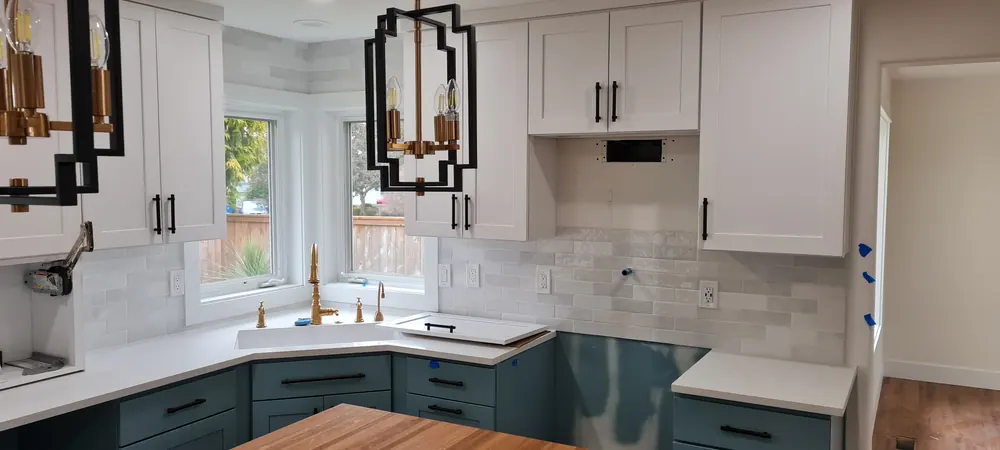 Kitchen with green lower cabinets, white uppers and brass pendants