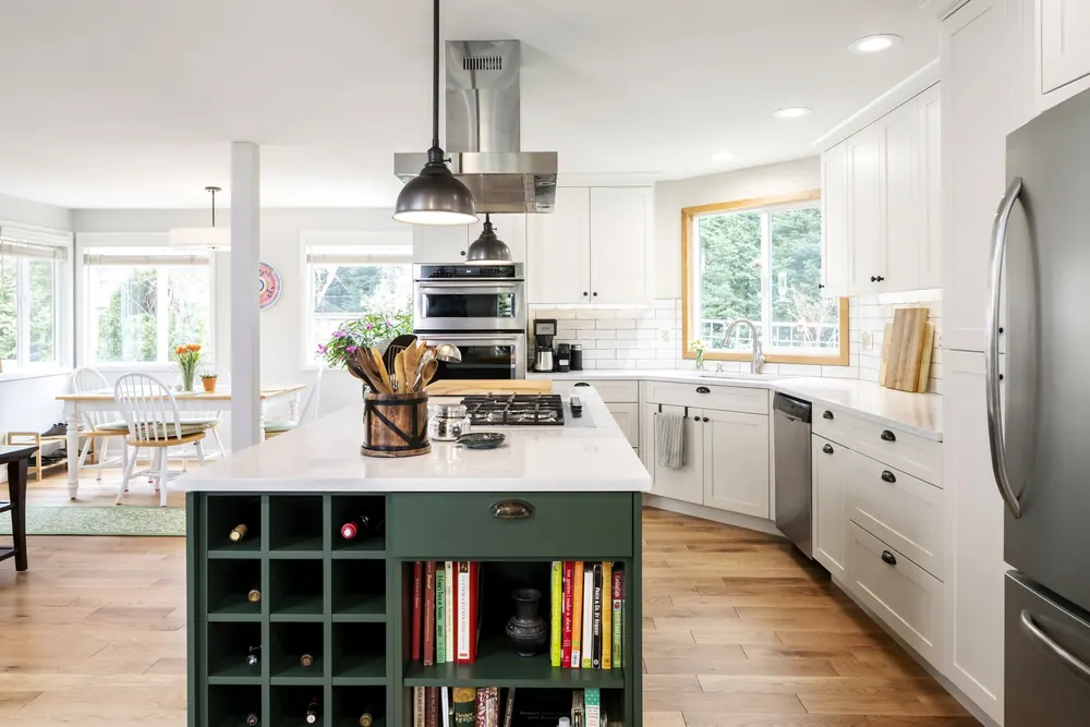 Green island with a bookshelf and wine cubbies, white cabinets beyond