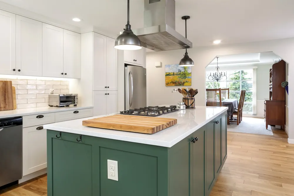 Green kitchen island with a pendant light and white perimeter cabinets