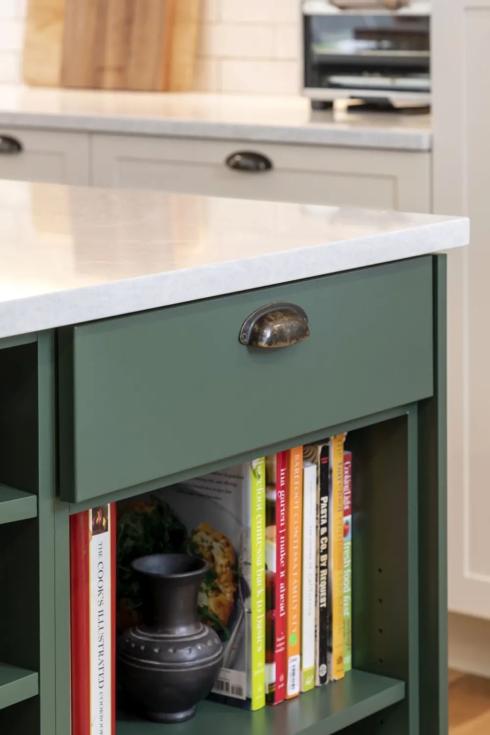 Open-shelf end of the green island with cookbooks