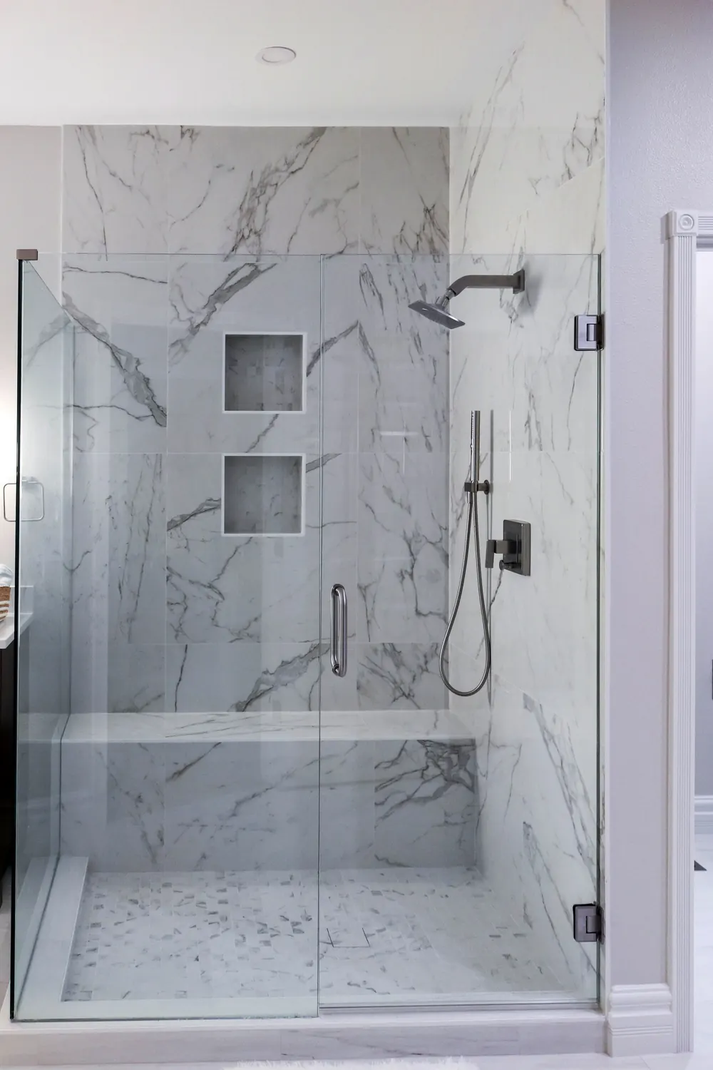 Marble-look tile shower with a built-in bench and niches