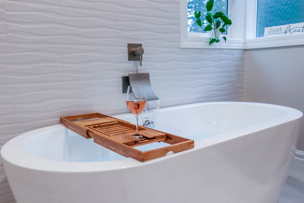Freestanding tub with a wood bath tray against textured white tile