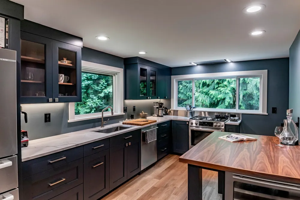 Navy kitchen cabinets, a walnut island and windows facing evergreen trees