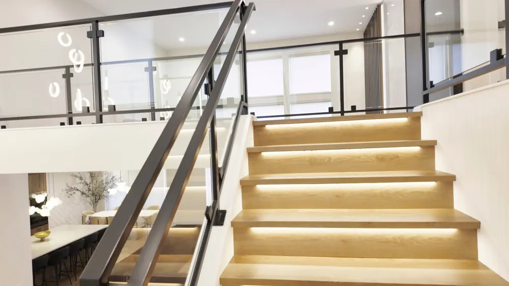 Staircase with lit wood treads and a black railing